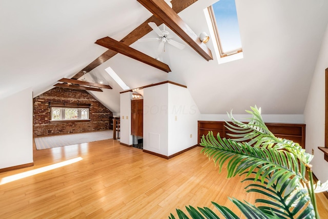 bonus room with vaulted ceiling with skylight, ceiling fan, wood finished floors, and brick wall