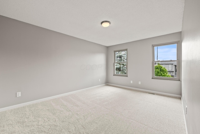 carpeted spare room with baseboards, a textured ceiling, and visible vents