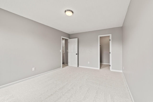 unfurnished bedroom with baseboards, a spacious closet, and light colored carpet