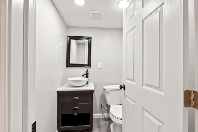 half bathroom featuring visible vents, vanity, wood finished floors, toilet, and baseboards