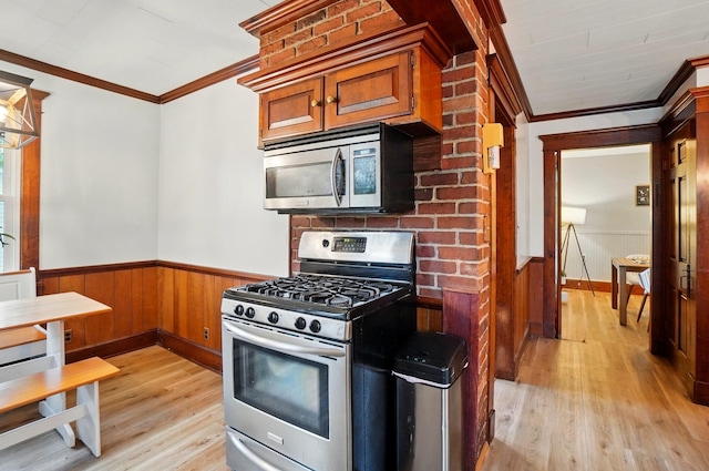 kitchen featuring light wood finished floors, stainless steel appliances, wainscoting, and crown molding