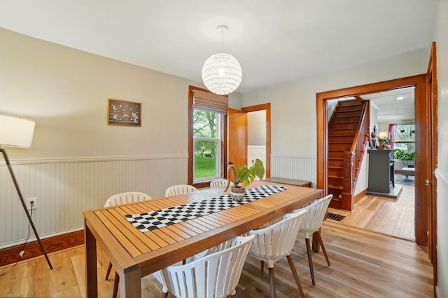 dining space featuring light wood finished floors, stairs, a wainscoted wall, and an inviting chandelier