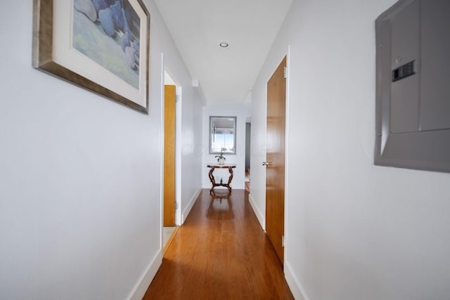 corridor featuring baseboards, wood finished floors, and electric panel
