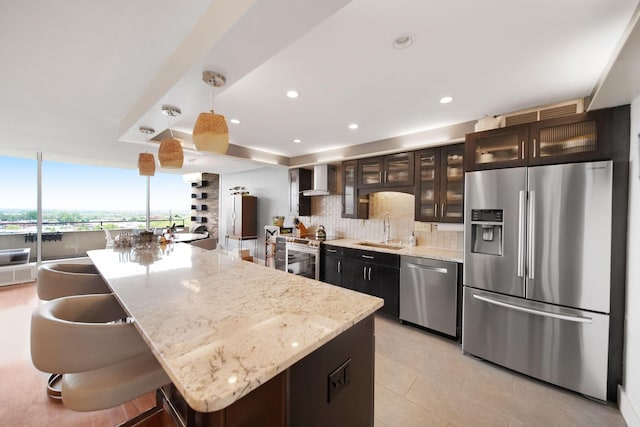 kitchen featuring a sink, wall chimney exhaust hood, stainless steel appliances, tasteful backsplash, and glass insert cabinets