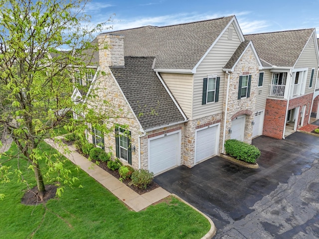 townhome / multi-family property with an attached garage, a shingled roof, aphalt driveway, and stone siding
