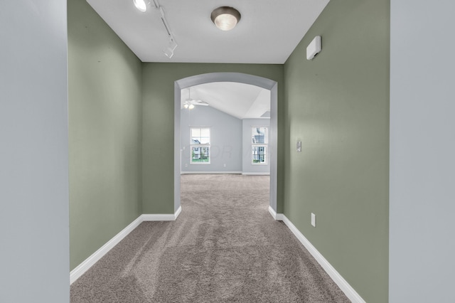 hall with track lighting, lofted ceiling, carpet flooring, baseboards, and arched walkways