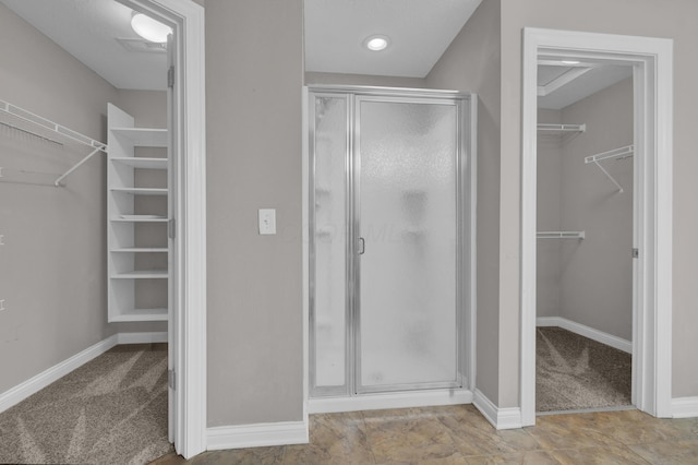 bathroom featuring baseboards, a walk in closet, a stall shower, and visible vents
