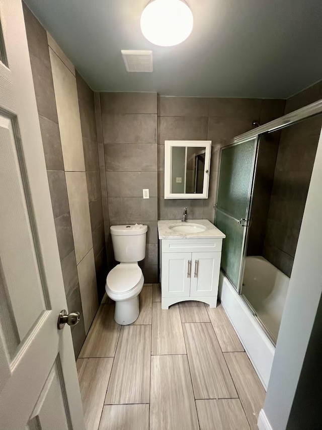 full bathroom with wood tiled floor, tile walls, vanity, combined bath / shower with glass door, and toilet