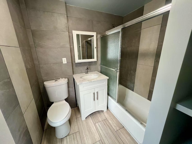 full bath featuring vanity, combined bath / shower with glass door, toilet, and tile walls