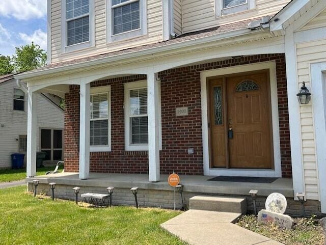 view of exterior entry featuring brick siding and a porch