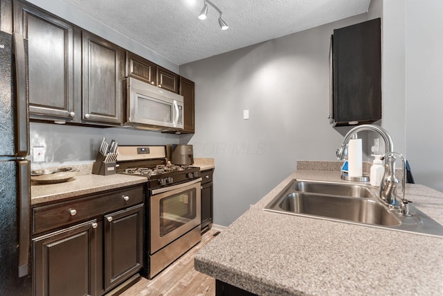 9137 Parkpoint Ln, Lewis Center, OH 43035 - kitchen featuring stainless steel appliances, a sink, light wood-type flooring, a textured ceiling, and dark brown cabinetry
