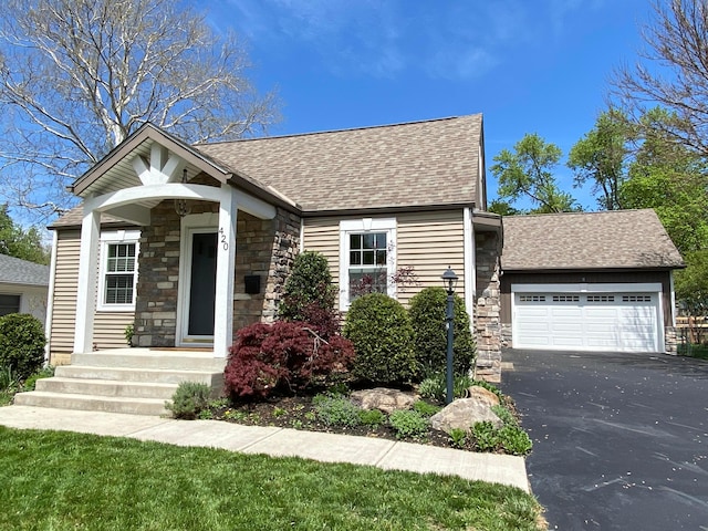 view of front of property featuring roof with shingles, an attached garage, driveway, and stone siding