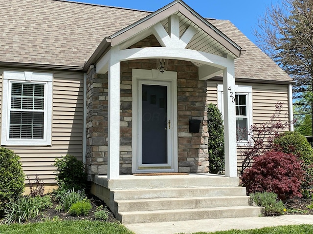 doorway to property featuring a shingled roof and stone siding