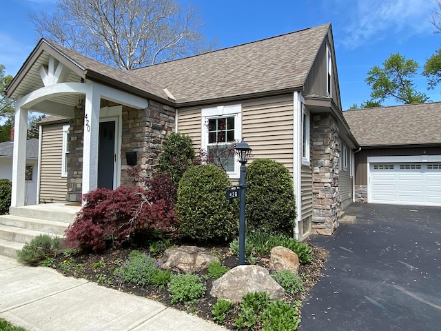 view of front of property with stone siding, roof with shingles, an attached garage, and asphalt driveway