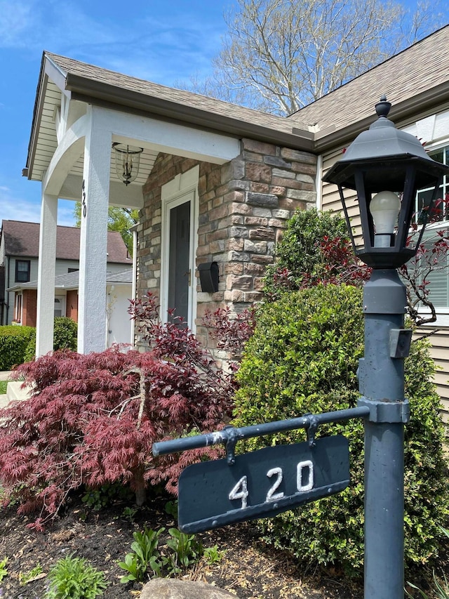 entrance to property featuring stone siding and a shingled roof