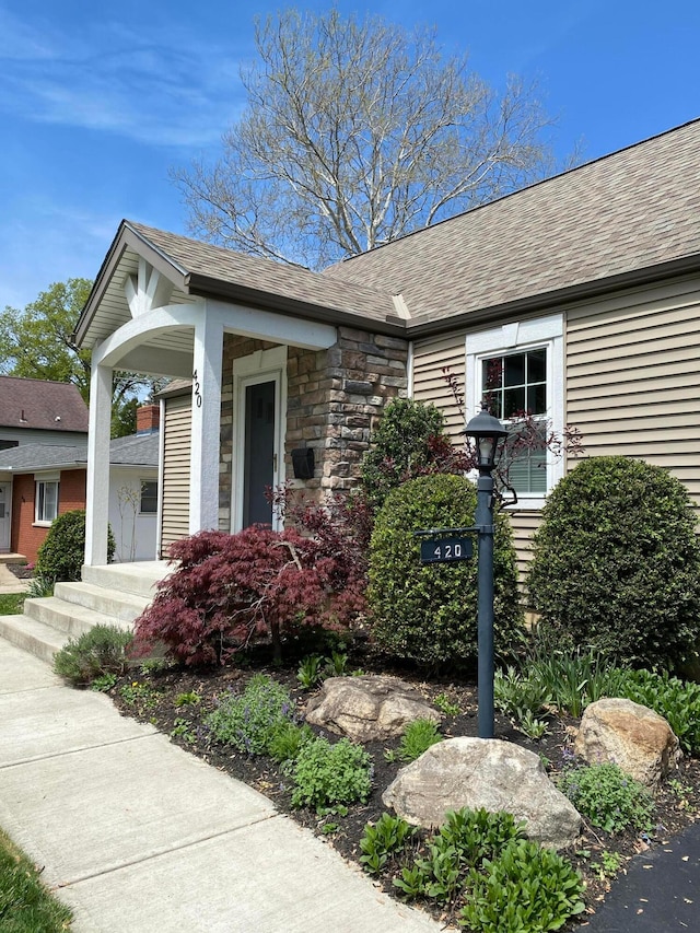 view of front of home with a shingled roof and stone siding