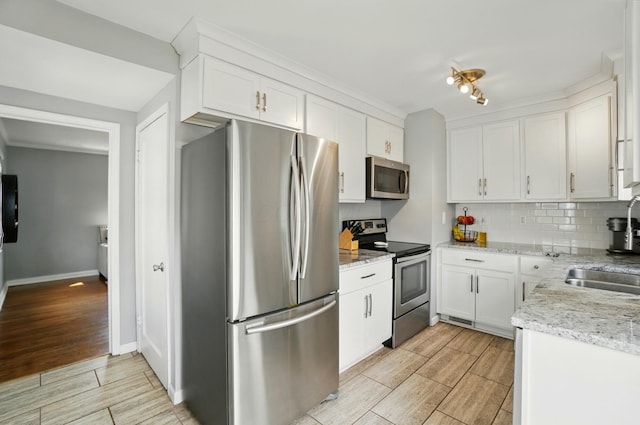 kitchen with baseboards, white cabinets, wood finish floors, tasteful backsplash, and appliances with stainless steel finishes