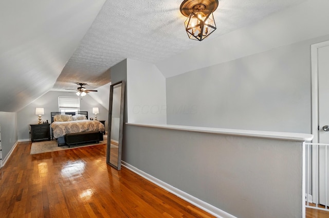 bedroom with vaulted ceiling, a textured ceiling, baseboards, and wood finished floors
