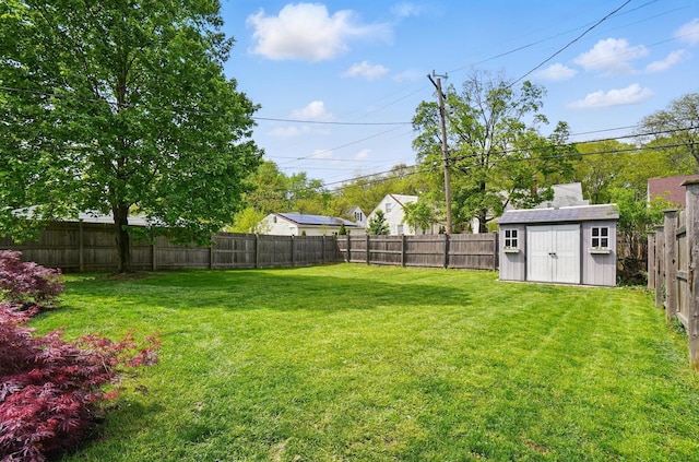 view of yard with a fenced backyard, a storage unit, and an outbuilding