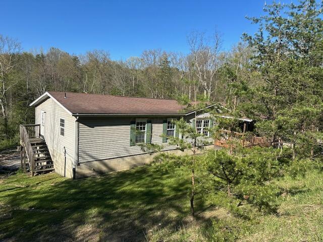 back of house featuring a lawn, a deck, a view of trees, and stairs