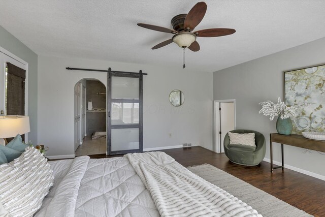 bedroom featuring visible vents, wood finished floors, baseboards, a barn door, and arched walkways