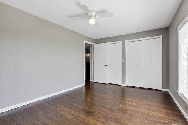 unfurnished bedroom featuring ceiling fan, baseboards, multiple closets, and wood finished floors