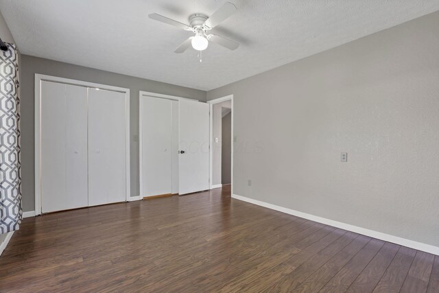 unfurnished bedroom with baseboards, a ceiling fan, dark wood-style flooring, and two closets