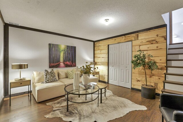 living area featuring visible vents, ornamental molding, wooden walls, dark wood-type flooring, and a textured ceiling
