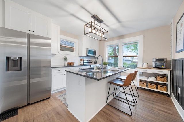 kitchen featuring stainless steel appliances, a sink, light wood-type flooring, white cabinetry, and a kitchen bar