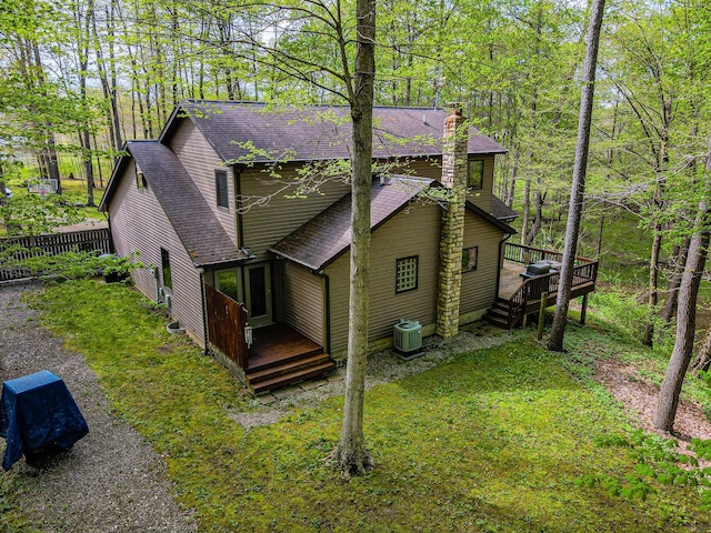 view of side of home with a deck, cooling unit, a chimney, and roof with shingles