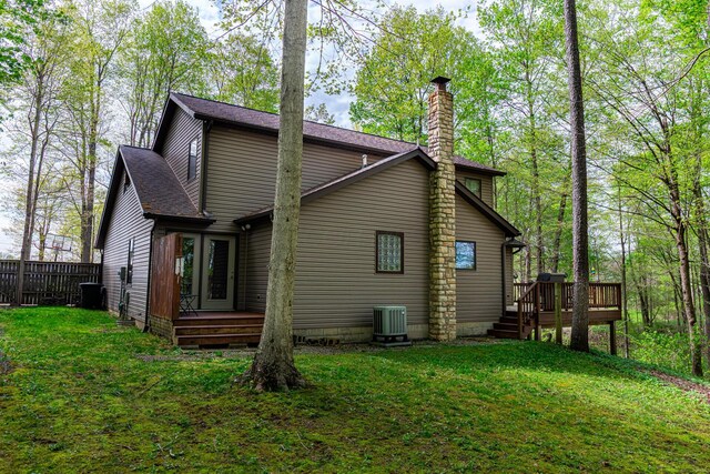 back of house with roof with shingles, a wooden deck, a chimney, central air condition unit, and a yard
