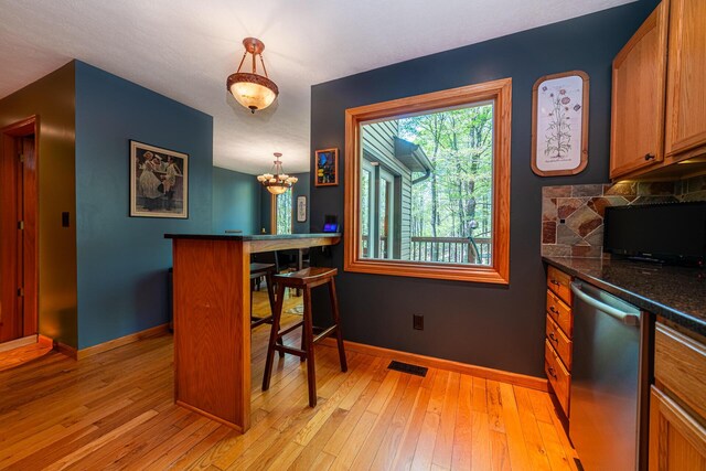 kitchen with dark countertops, dishwasher, brown cabinetry, light wood-style flooring, and baseboards