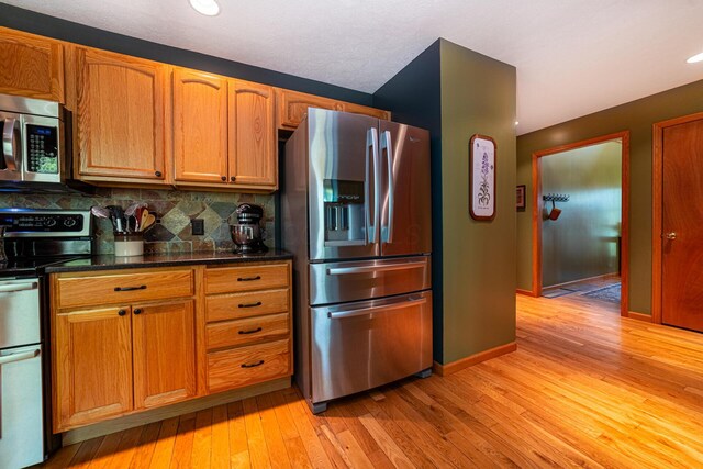 kitchen with brown cabinets, backsplash, stainless steel appliances, and light wood-type flooring
