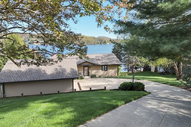 view of front of home with a water view, a front yard, a shingled roof, and curved driveway