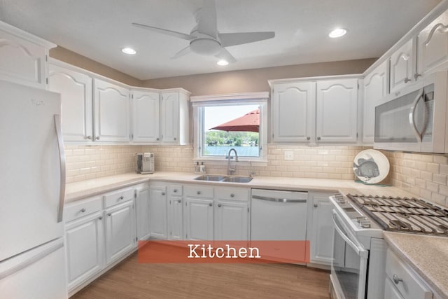 kitchen with a sink, white appliances, ceiling fan, light wood finished floors, and white cabinets
