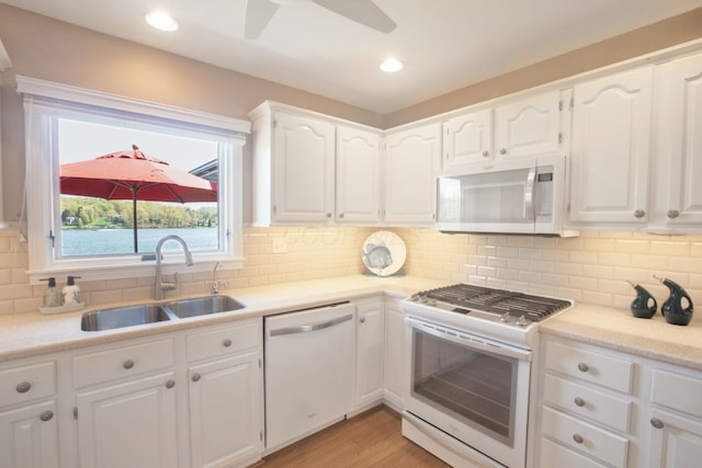 kitchen with white appliances, white cabinets, ceiling fan, and a sink