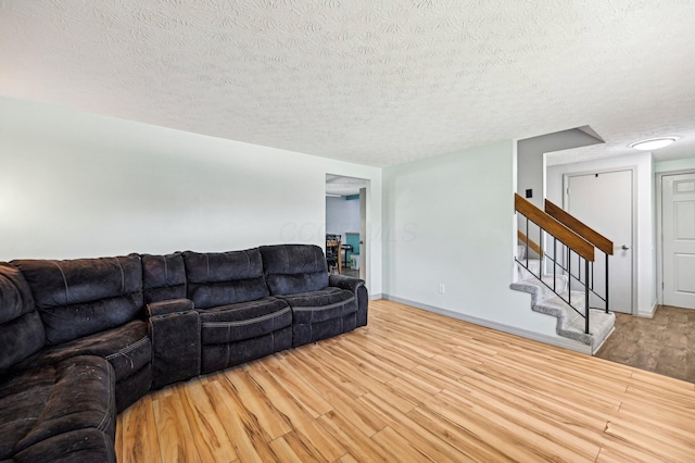 living room with stairway, a textured ceiling, baseboards, and wood finished floors