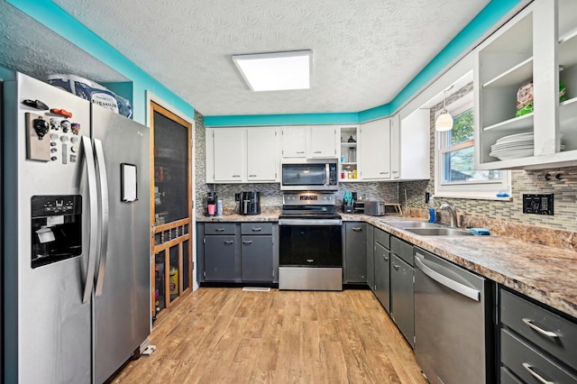 kitchen with open shelves, light wood-type flooring, white cabinets, a sink, and stainless steel appliances