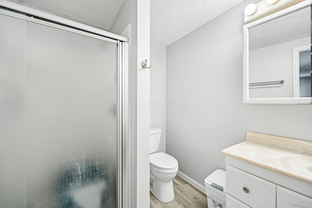 full bathroom with vanity, wood finished floors, toilet, baseboards, and a stall shower