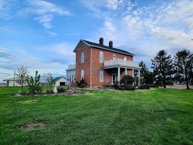 exterior space featuring a balcony, a chimney, a lawn, and brick siding