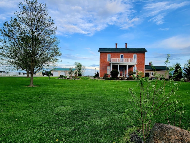 rear view of house with a lawn, a balcony, and brick siding