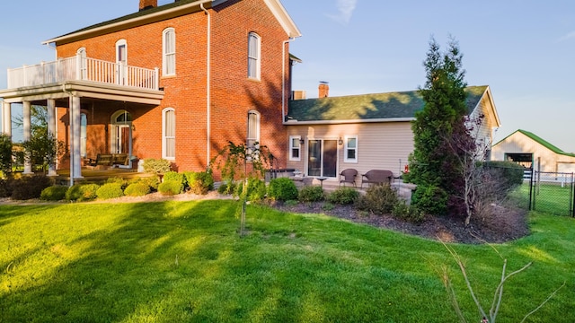rear view of house featuring a chimney, brick siding, fence, a balcony, and a yard