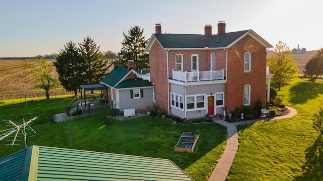 rear view of house with brick siding, entry steps, a chimney, a balcony, and a yard