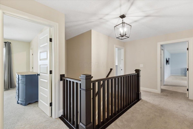 hallway with an upstairs landing, light carpet, a chandelier, and baseboards