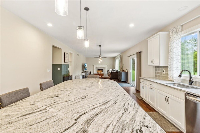 kitchen with a sink, dishwasher, a fireplace, light stone countertops, and dark wood finished floors