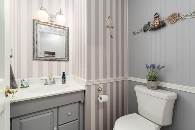 half bathroom with vanity, toilet, and wallpapered walls
