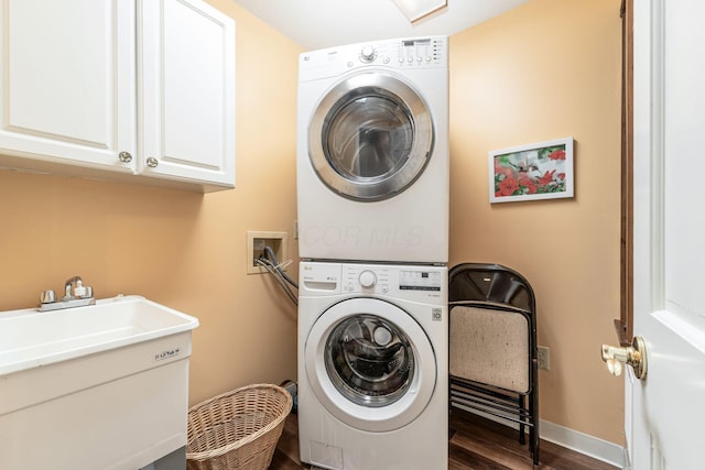 clothes washing area with stacked washer and clothes dryer, baseboards, dark wood finished floors, a sink, and cabinet space