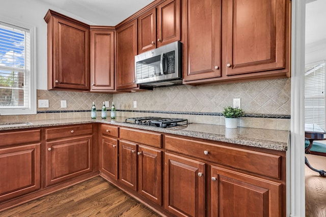 7169 Fernridge Dr, New Albany, OH 43054 - kitchen with stainless steel microwave, black gas cooktop, dark wood finished floors, light stone countertops, and decorative backsplash