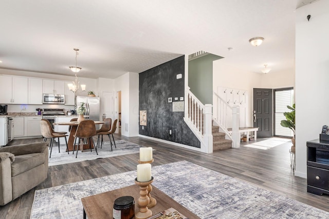 living area with stairway, a chandelier, wood finished floors, baseboards, and an accent wall