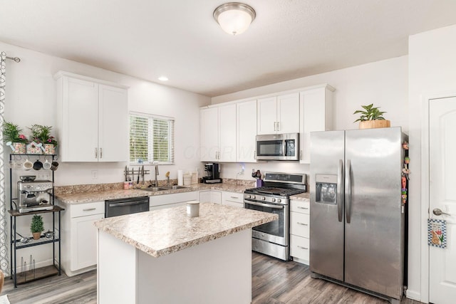 kitchen featuring stainless steel appliances, a sink, wood finished floors, a kitchen island, and white cabinets